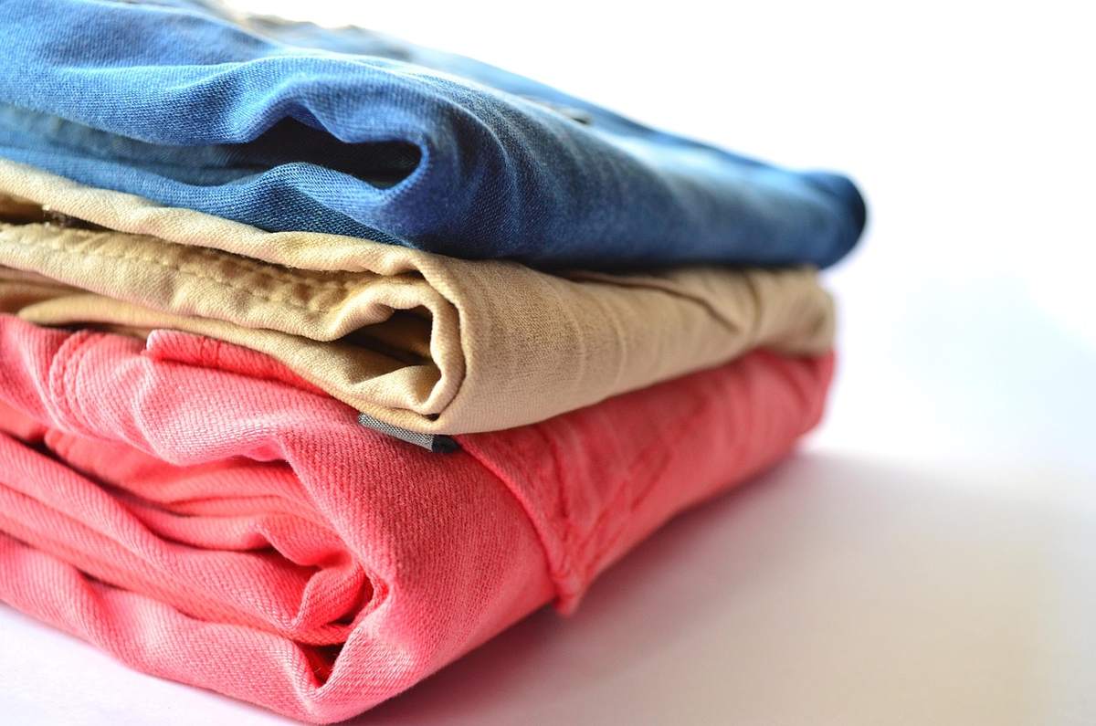 Trois chemises pliées, une bleue, une beige, une rose, sur fond blanc