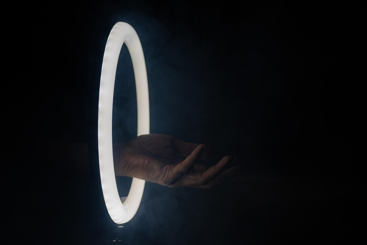 Main droite sortant d'un cercle lumineux contre fond noir