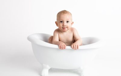 Bébé nu dans une baignoire blanche, posé sur les bords, souriant