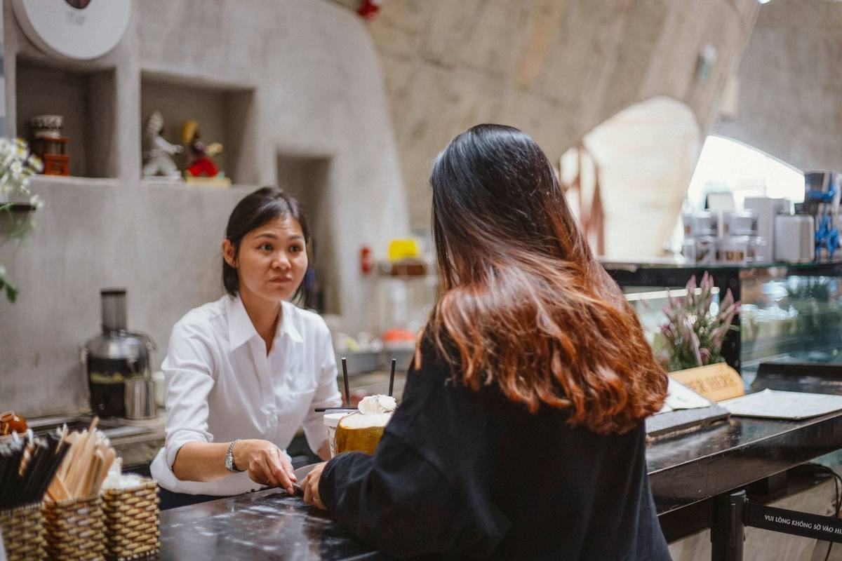 Femme en noir commande à une serveuse en blouse blanche dans un café décoré