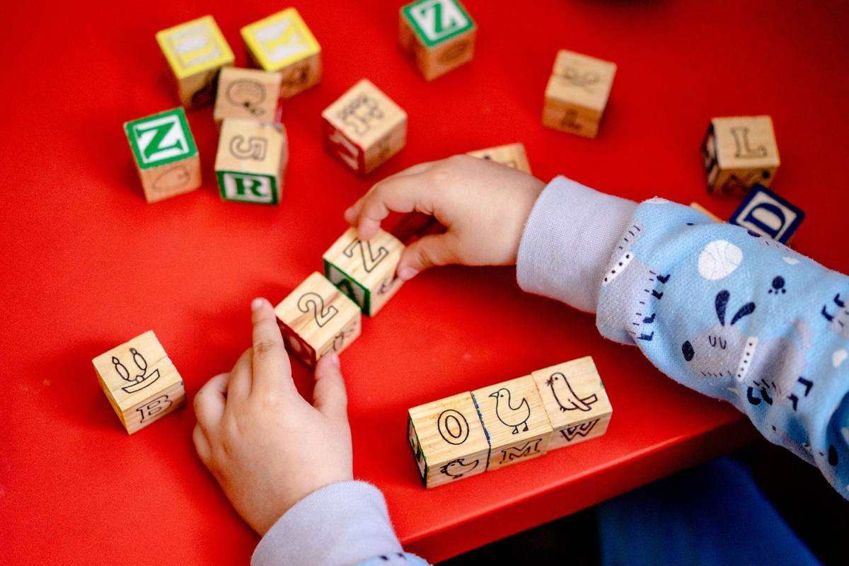 Enfant manipulant des blocs en bois avec lettres et chiffres sur une table rouge