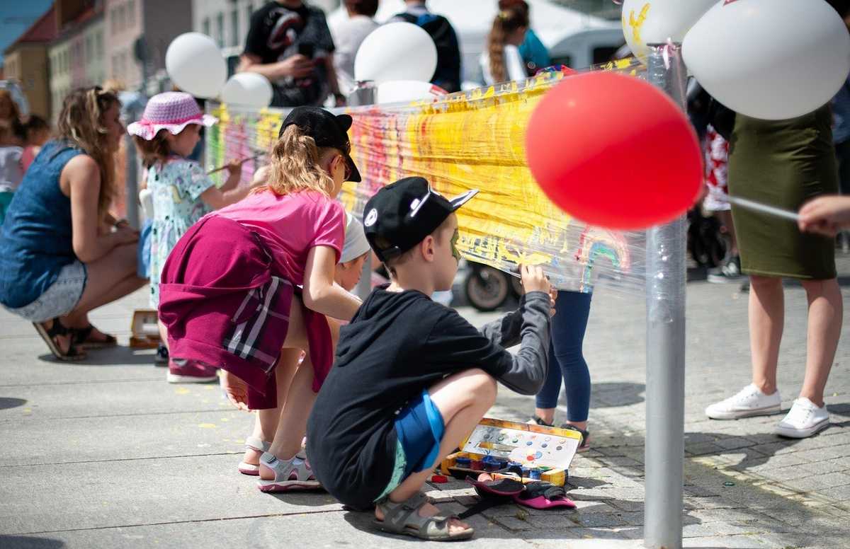 Enfants regardent un spectacle de rue avec ballons et affiche jaune