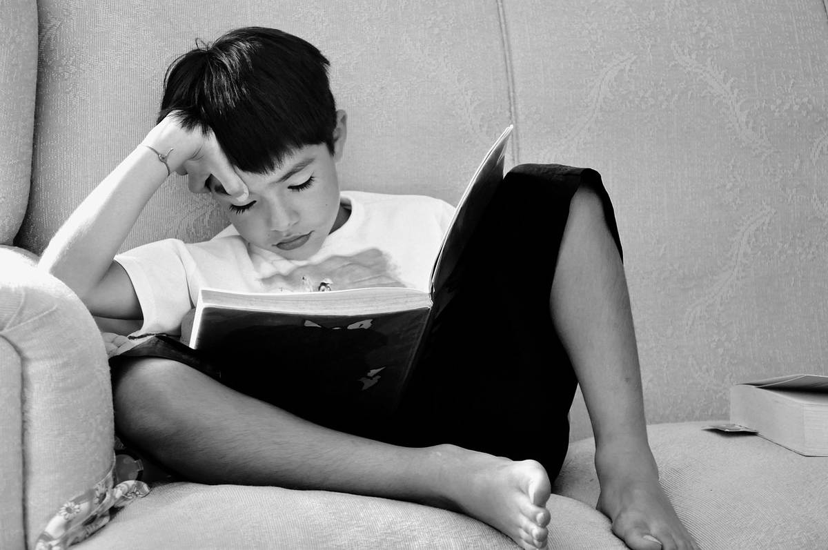 Un enfant assis sur un canapé, lisant un livre, la main sur le front