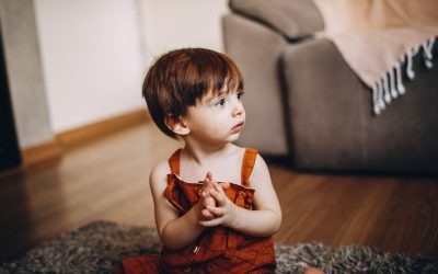 Petit enfant assis sur un tapis, mains jointes, regard vers le haut