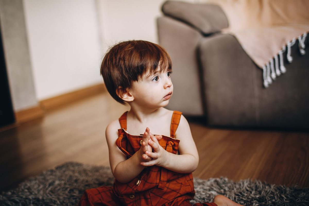 Petit enfant assis sur un tapis, mains jointes, regard vers le haut