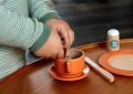 Un enfant verse du contenu d'une petite cuillère dans une tasse orange