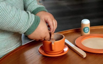 Un enfant verse du contenu d'une petite cuillère dans une tasse orange