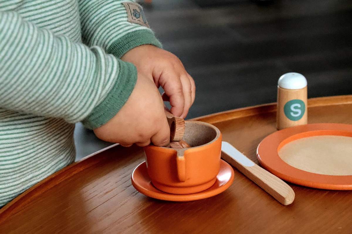 Un enfant verse du contenu d'une petite cuillère dans une tasse orange