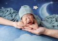 Un bébé en bonnet bleu pleure dans les bras d'un adulte