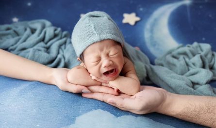 Un bébé en bonnet bleu pleure dans les bras d'un adulte
