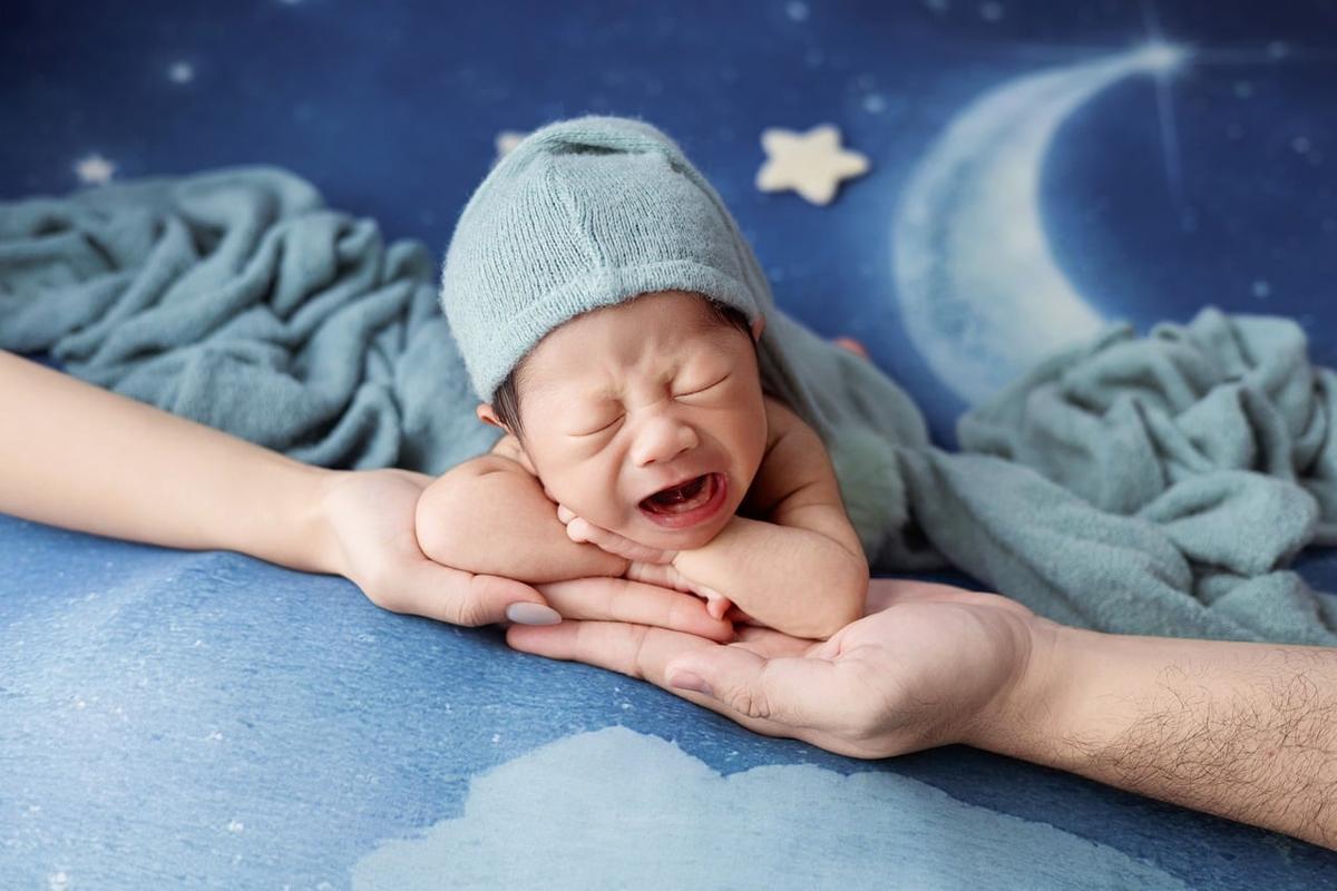 Un bébé en bonnet bleu pleure dans les bras d'un adulte