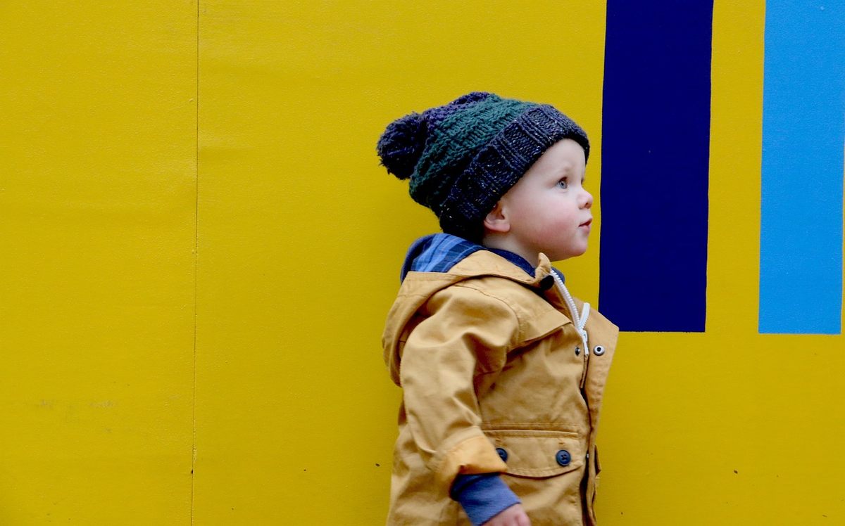 Un petit garçon en bonnet et veste jaune regarde à droite