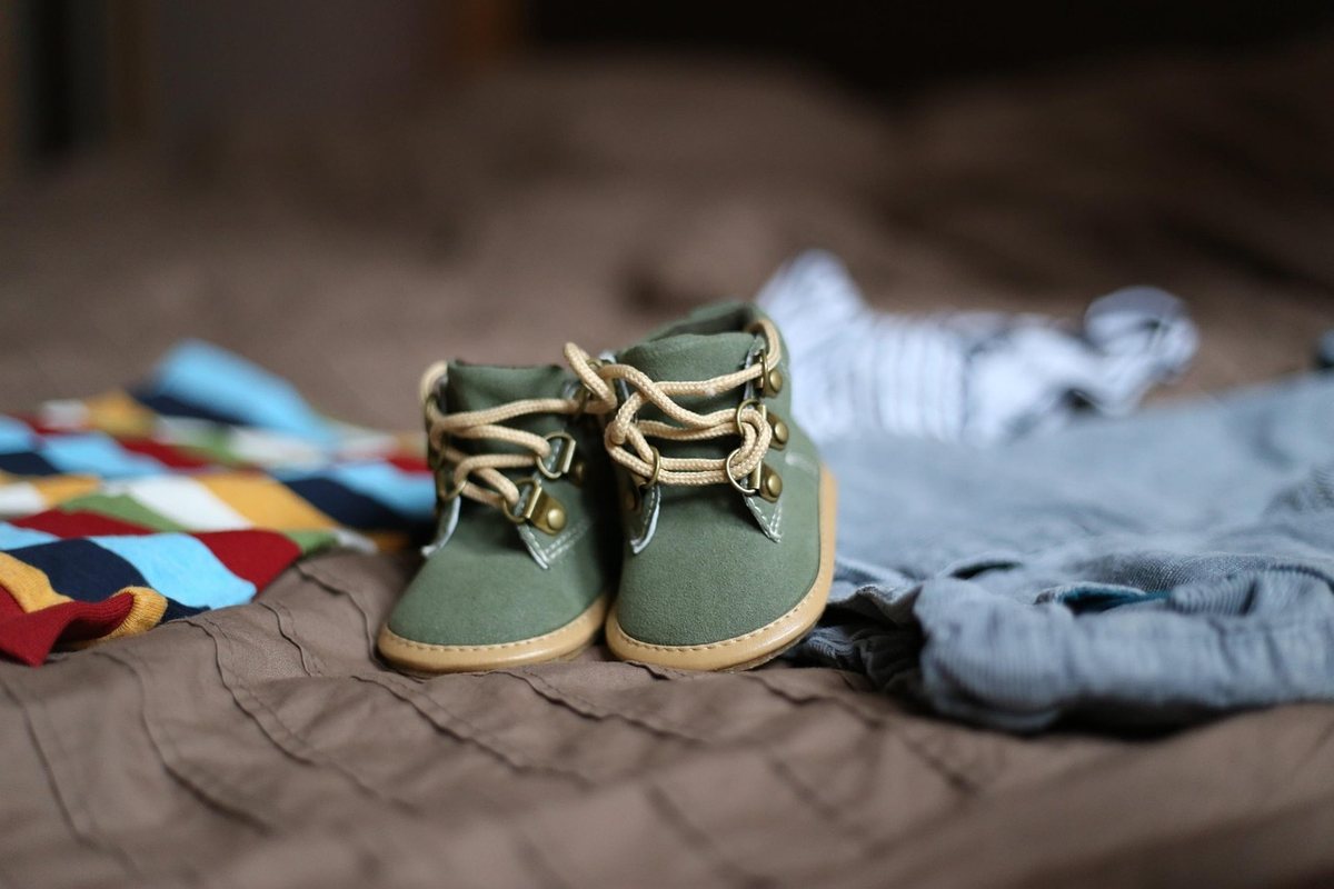 Petites chaussures vertes et vêtements disposés sur un lit doux