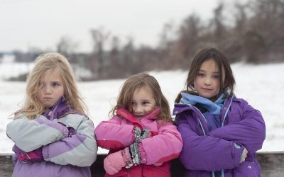 Trois jeunes filles en manteaux d'hiver se tiennent les bras croisés