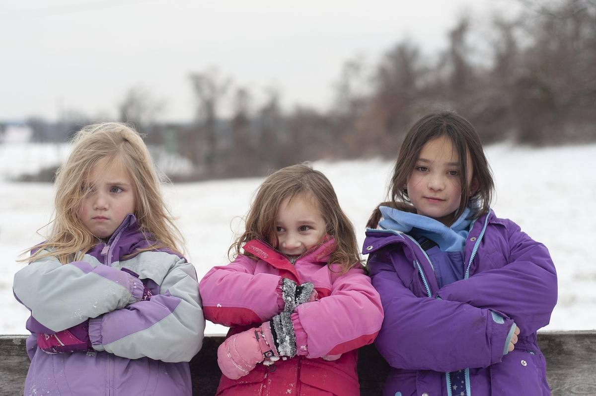 Trois jeunes filles en manteaux d'hiver se tiennent les bras croisés