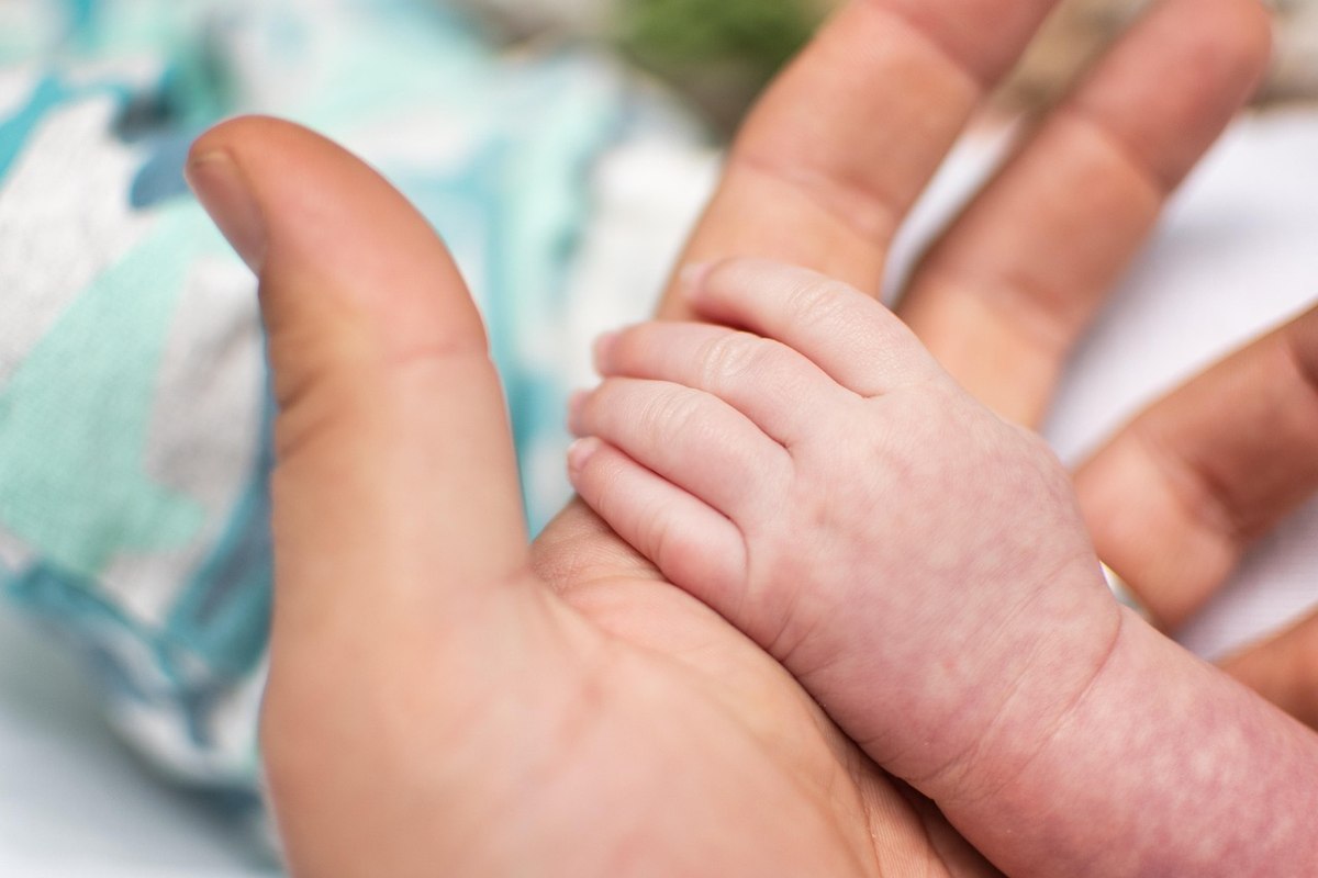 main d'adulte soutient doucement la petite main du bébé