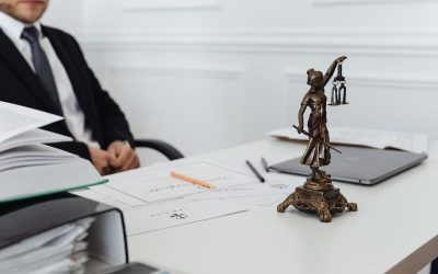 Homme en costume assis à un bureau avec une statue de la justice, des papiers et un ordinateur portable