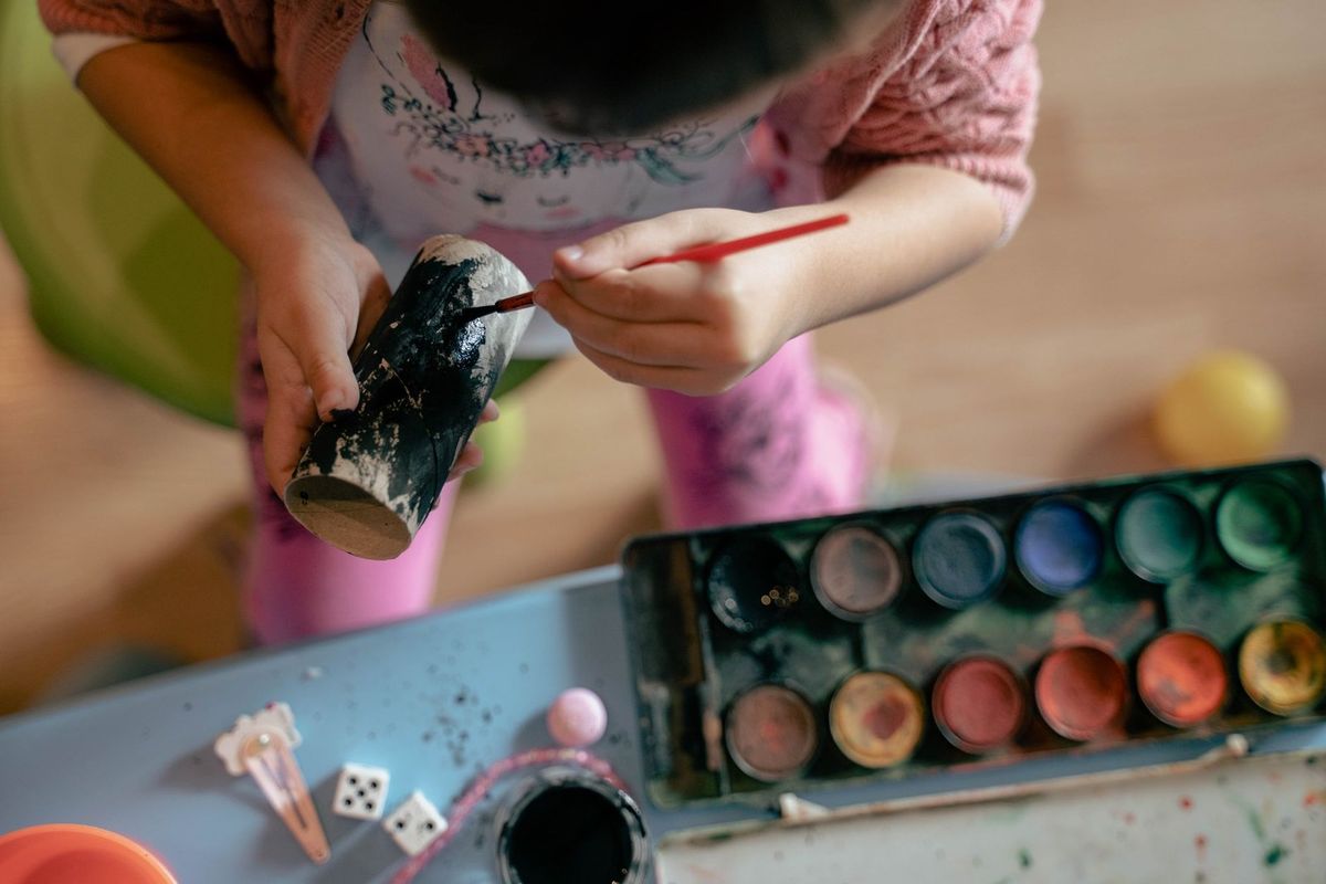 Enfant utilisant un pinceau pour peindre, à une table avec des peintures et des jouets