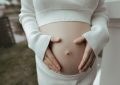 Une femme enceinte en blanc caresse doucement son ventre arrondi