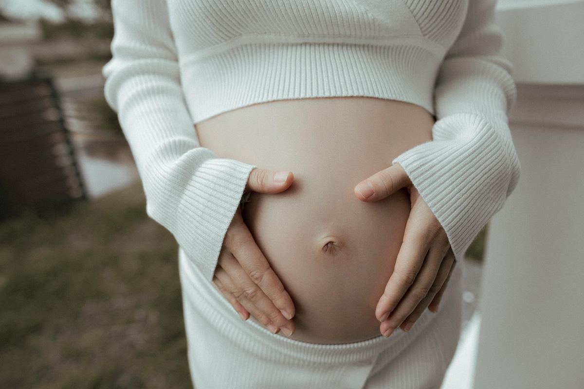 Une femme enceinte en blanc caresse doucement son ventre arrondi
