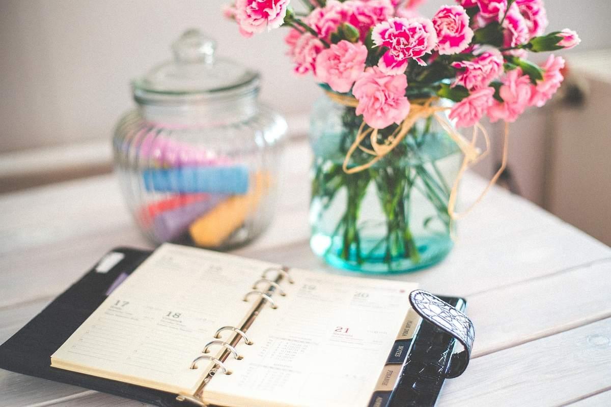 Carnet ouvert sur une table blanche avec un vase de fleurs roses à côté
