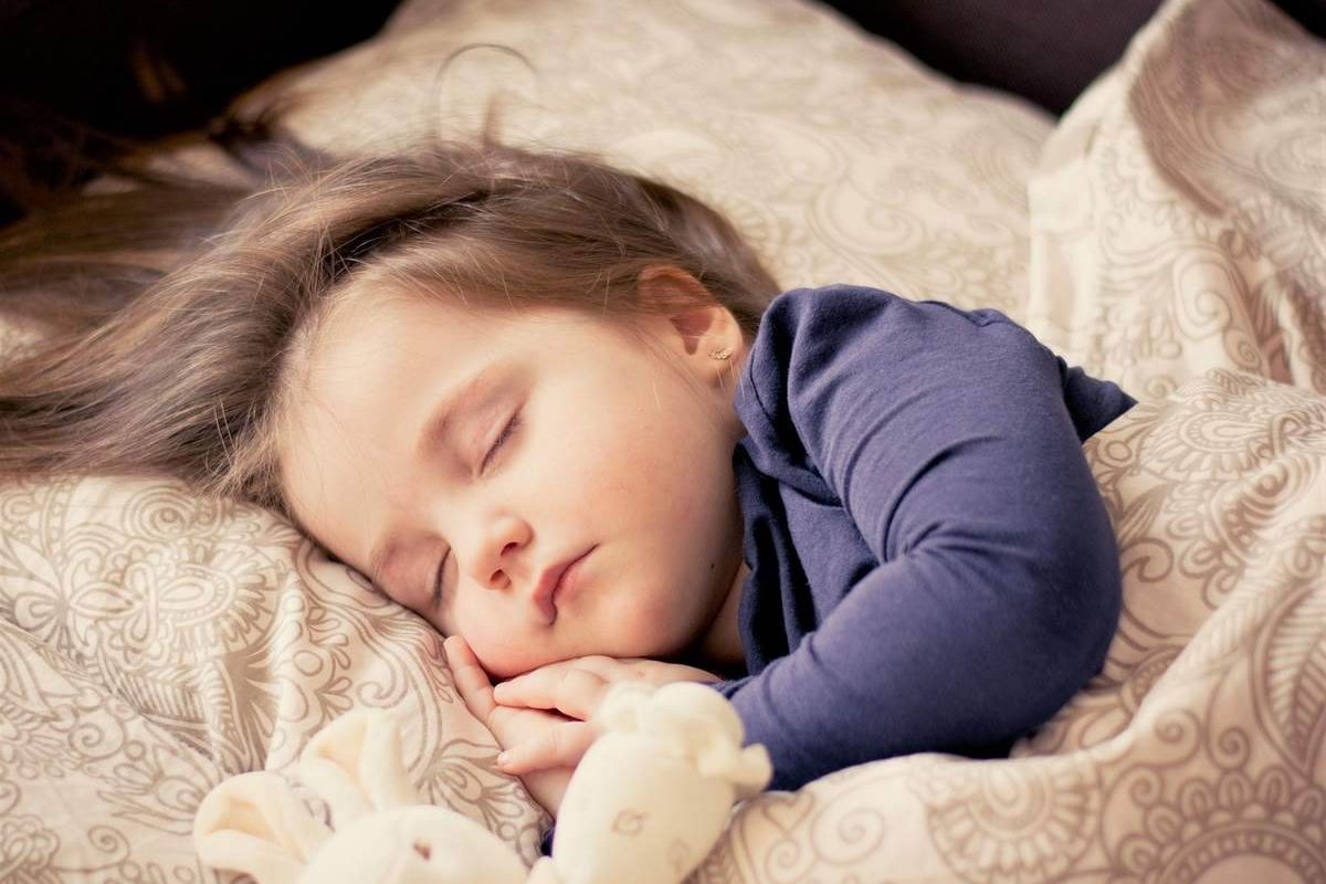 Une enfant dort paisiblement sur des coussins à motifs beiges et bleus